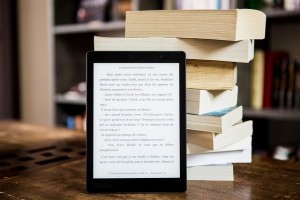 Photo d'une tablette numérique contenant des ebooks et plusieurs livres sur une table