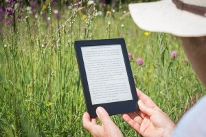 Photo d'une personne assise dans l'herbe lisant un ebook avec une liseuse